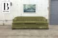 Olive green tufted sofa in front of a white brick wall with a nautical painting.