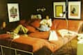 Retro room with large orange bed, two people relaxing, wall art, books, and vintage lamps.