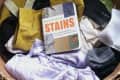 Basket of assorted laundry with a book titled "Field Guide to Stains" on top.