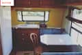 Camper kitchen with wooden cabinets, a white sink, small dining table, and a window with blinds.