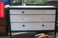 Worn white dresser with black knobs and green trim, labeled "Before."