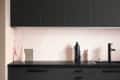 Modern kitchen with black cabinets, pink tile backsplash, black faucet, and decorative vases on the counter.