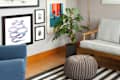 Gallery wall with colorful art, gray armchair, gold floor lamp, potted plant, and striped rug in a cozy corner.
