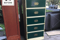 Green and beige five-drawer dresser on a wooden deck, next to a brown cabinet door.