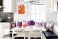 Kitchen nook with white table, purple cushions, pink drinks, and a floral centerpiece under a modern pendant light.