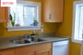 Yellow kitchen with wooden cabinets, double sink, and plants on the windowsill.