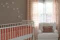 Nursery with white crib, butterfly wall decor, pink curtains, white armchair, and a floral pendant light.