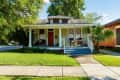 Charming bungalow with a front porch, rocking chairs, and lush greenery.