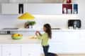 Child peeling orange at white kitchen island with yellow pendant lamp and colorful shelves.