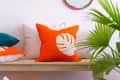 Yellow pendant light, orange leaf pillow on bench, round mirror, and colorful baskets on woven rug with green plant.