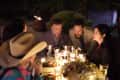 People gathered around a candlelit dinner table outdoors, engaged in conversation.