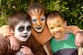 Three children with face paint resembling a panda, tiger, and giraffe, smiling outdoors.