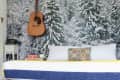 Bedroom with snowy forest mural, acoustic guitar on wall, bed with books, and shoes on striped rug.