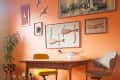 Mid-century modern dining area with orange walls, wooden table, yellow chair, and eclectic wall art.