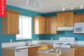 Wooden kitchen cabinets with teal walls, white appliances, and a central island under track lighting.