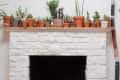 A white brick fireplace with several terra cotta pots with plants on top of the mantel