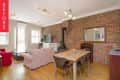 Open-plan living and dining area with exposed brick wall, beige sofa, wooden dining table, and modern lighting.