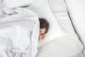 Person sleeping under white bedding, head resting on a pillow.