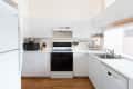 Modern kitchen with white cabinets, black stove, microwave, knife block, and stainless steel sink on wooden floor.