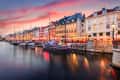 Colorful buildings and boats along Nyhavn canal in Copenhagen at sunset, with vibrant sky and reflections in the water.