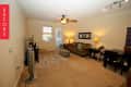 Living room with beige carpet, brown sofa, TV, ceiling fan, and dining table with chairs.