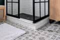 Black-framed glass shower with white subway tiles, patterned floor, and wooden cabinet in a modern bathroom.