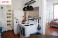 Small kitchen with white fridge, vintage stove, hanging pans, spice rack, and view into a bedroom with wooden floors.