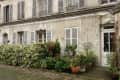 Facade of an old building with shuttered windows, potted plants, and cobblestone courtyard.