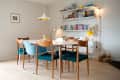 Dining room with wooden table, mixed chairs, pendant light, bookshelf filled with books, and a yellow lamp.