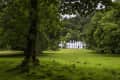 White castle with arched windows surrounded by lush green trees and grass.