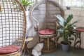 Wicker chairs with red cushions in a sunroom, surrounded by plants and string lights.