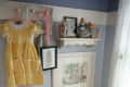 Vintage nursery corner with yellow dress, framed art, dolls, ironing board, and doll cradle on carpet.