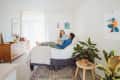 Couple relaxing on a bed in a bright bedroom with plants, wooden dresser, and colorful wall art.