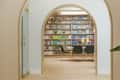 Arched entryway leading to a library with color-coordinated bookshelves, a table, and four dark green chairs.