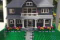 Two-story LEGO house with gray siding, white windows, and colorful flower garden on green base.