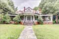 Historic Victorian house with wraparound porch, red brick chimneys, and lush greenery.