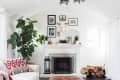 Living room with a white sofa, brown ottoman, fireplace, framed photos, and a large plant.