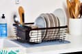 Dish rack with plates, mugs, and utensils on a kitchen counter, next to dish soap and a utensil holder.