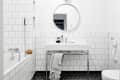 Modern bathroom with white subway tiles, round mirror, black hexagonal floor tiles, and a bathtub with a sponge.