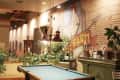 Pool table in a cozy room with brick walls, vintage decor, plants, and a mural of a chicken with "Farm" text.