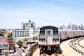 Subway train on elevated tracks with city skyline and buildings in the background.