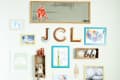 Gallery wall with framed art, wooden letters "JCL," plush toys, and colorful blocks on a red bench with pillows.