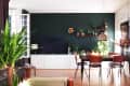 Living room with dark green accent wall, TV, white cabinet, dining table, wooden chairs, and various potted plants.