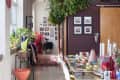 Dining area with colorful chairs, a long table set with dishes, hanging plants, and framed photos on the wall.