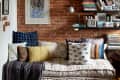 Daybed with patterned cushions, brick wall, bookshelves, and framed art in cozy living room.