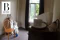 Cluttered room with wooden chair, cleaning supplies, and a small table with cups near a window.