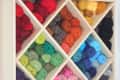 Wooden shelf with colorful yarn balls in diamond-shaped cubbies, jars of buttons on top, and storage pockets below.