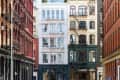 Historic New York City street with red, white, and beige buildings featuring fire escapes and arched windows.