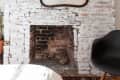Whitewashed brick fireplace with ornate mirror, black chair, and patterned rug.