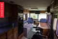 Interior of an RV with a blue sofa, wooden cabinets, desk, and large windows, labeled "Before."
